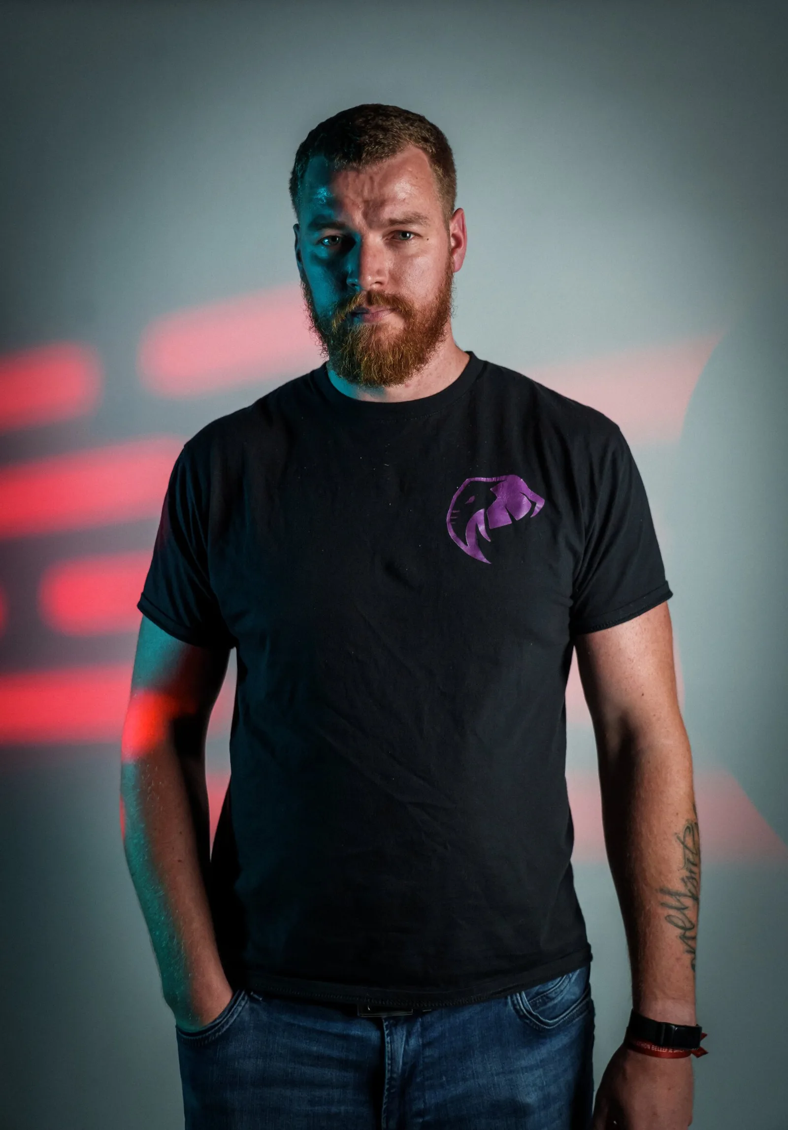 Man met baard in zwart shirt voor een lichte achtergrond met rode lichtstrepen