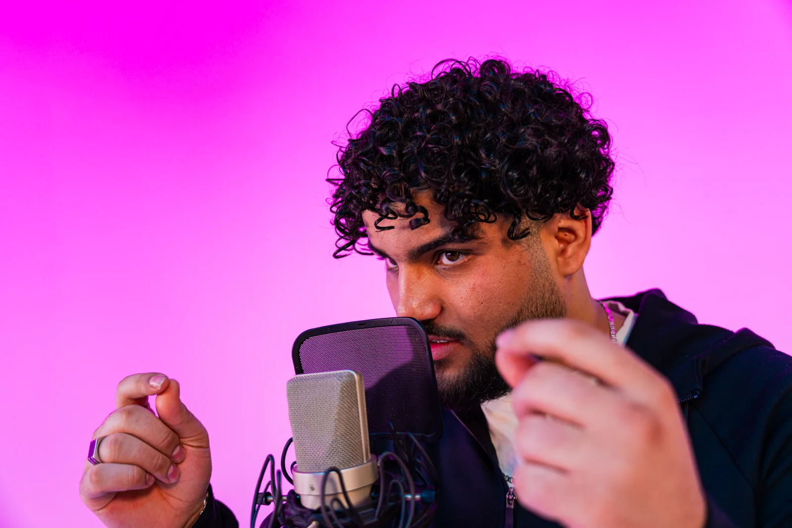 Rapper met krullen achter de microfoon voor een roze achtergrond
